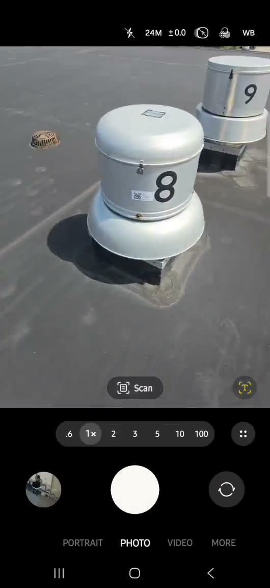 A phone camera pointed at a QR tag on a rooftop exhaust fan